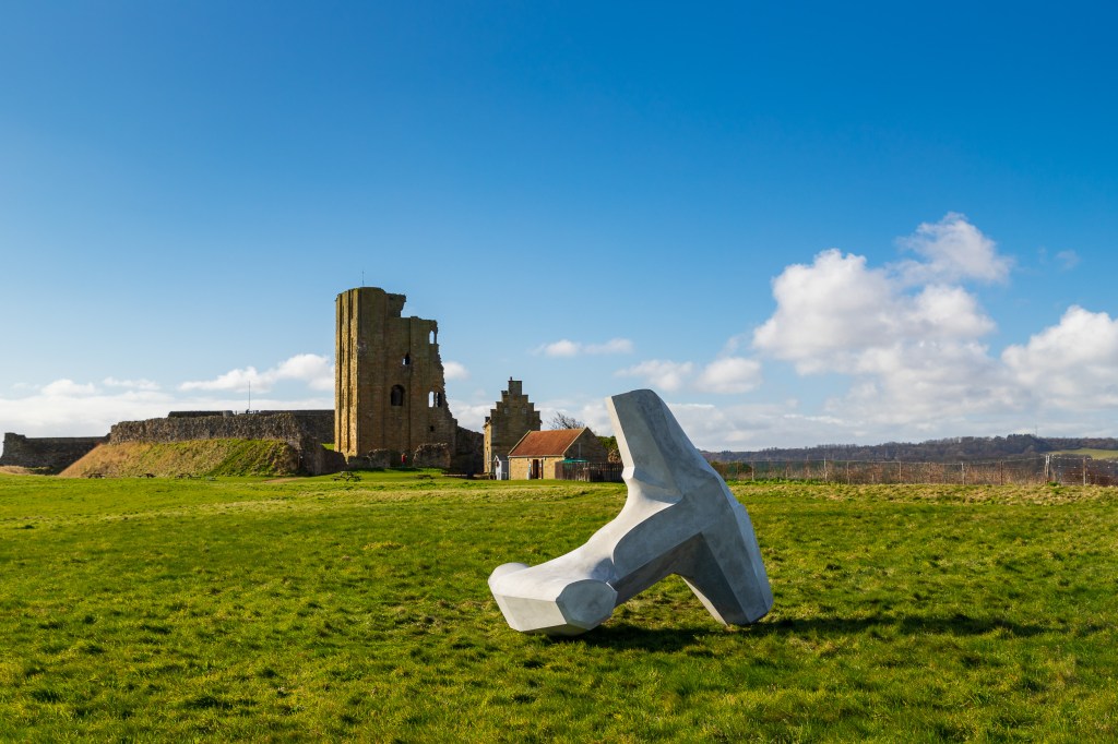 a scultpure which looks like a dolos on grass by a castle